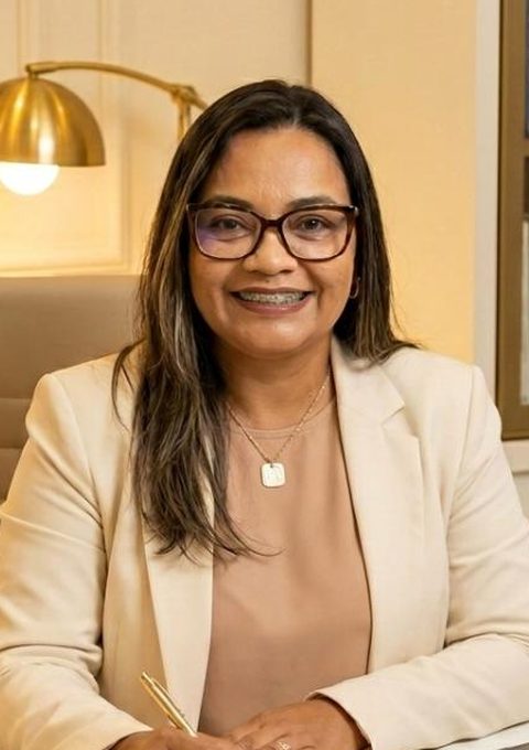 Ana Cristina Lovato sorrindo, sentada à mesa do consultório