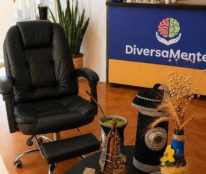 Consultório do DiversaMente: poltrona de couro, balcão de recepção azul com a logo, plantas e uma cuia de chimarrão